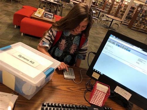 A student checks out a STEM kit in a clear plastic tub