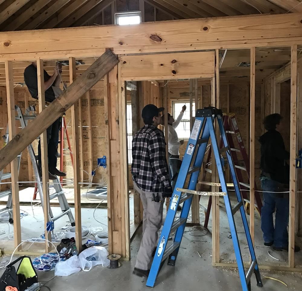 Academy students watch as an instructor shows them how to wire a building.